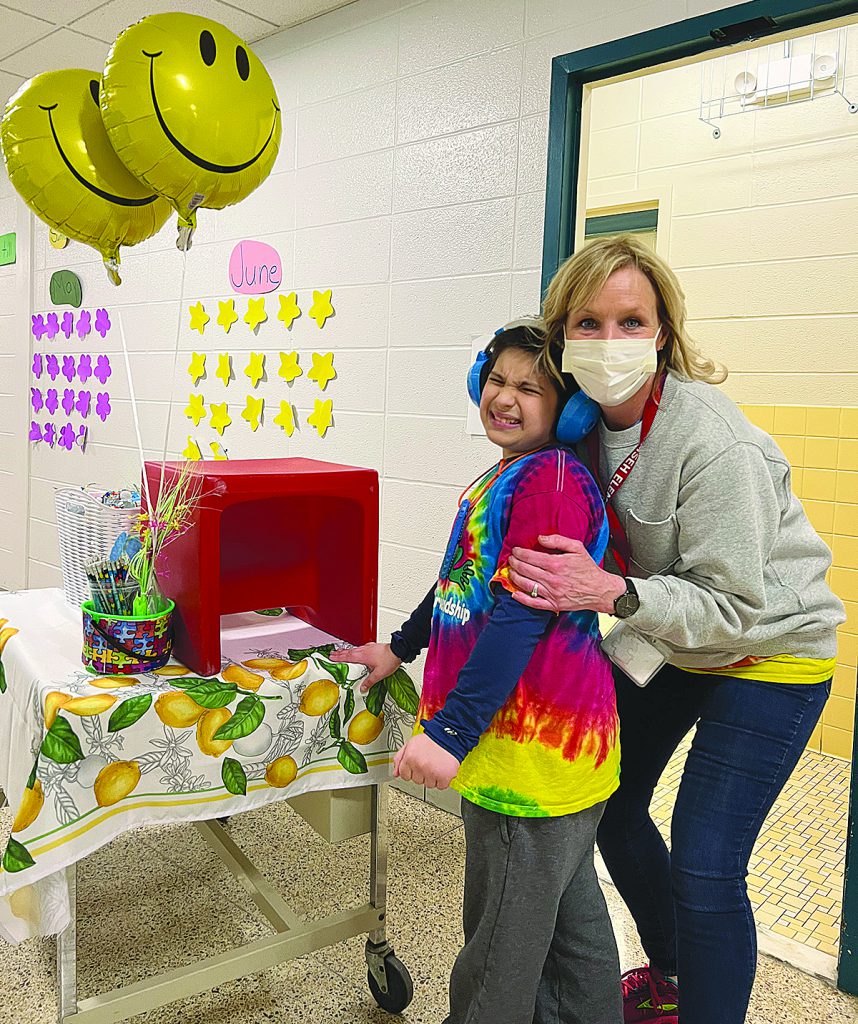 Teacher and student standing by table decorated for lemonade stand. 