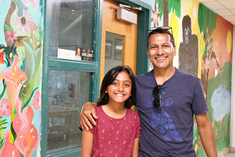 a father and daughter stand in art hallway and pose for a photo.