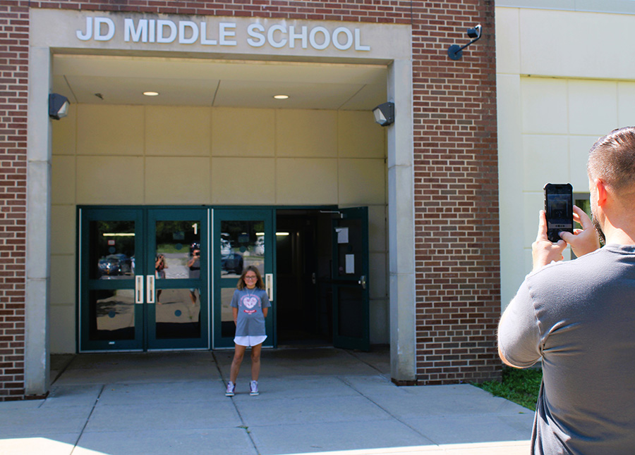 a parent takes a photo of his daughter in front of the middle school entrance. 