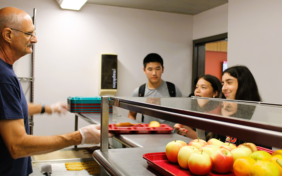 Food Services staff member hands out food trays to students in high school lunch line.