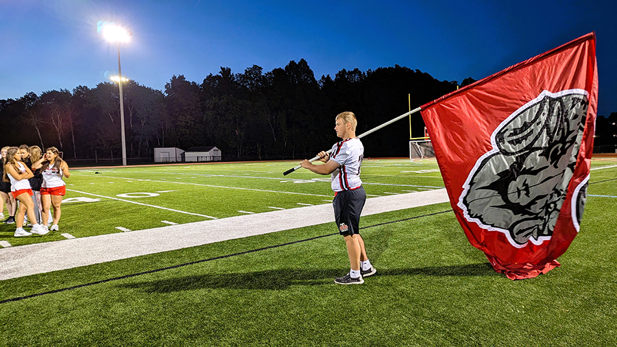 J-DHS football player stands next to field holding battle flag. 