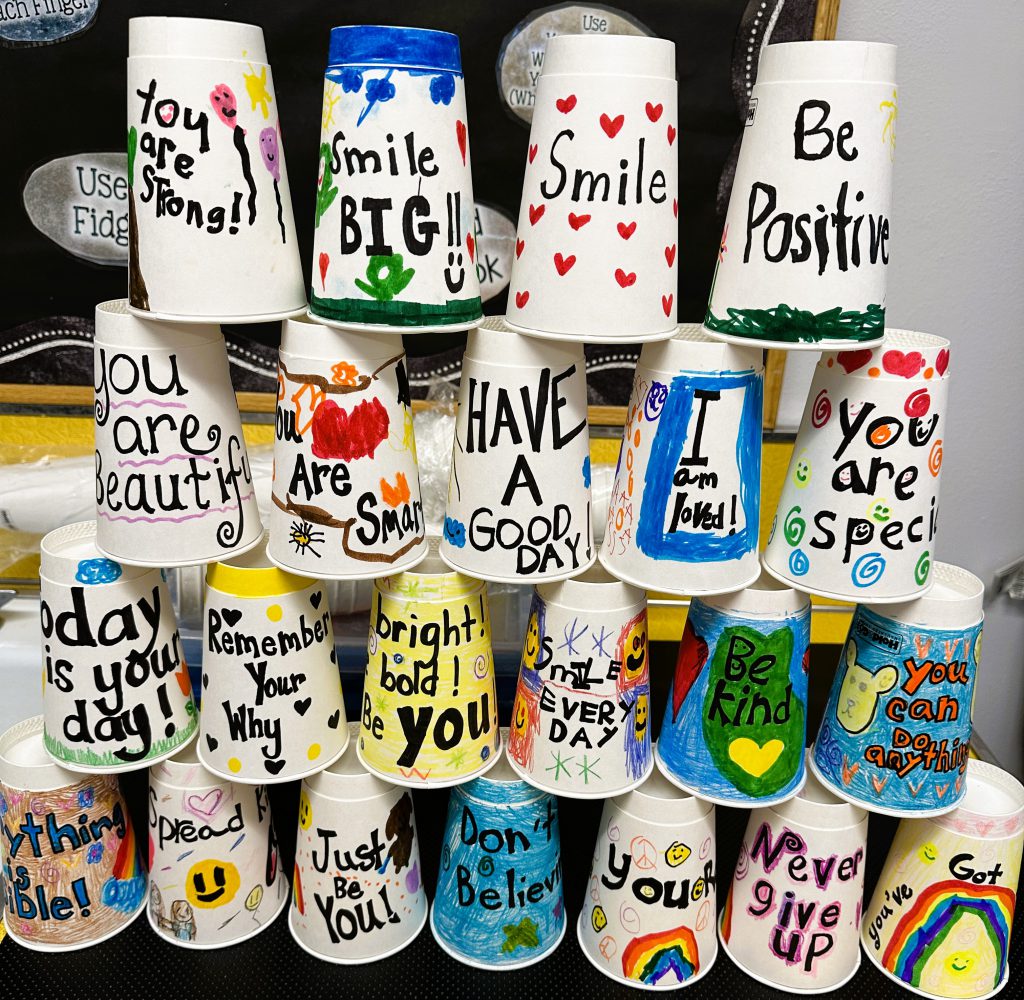 Close up of stacked decorated coffee cups with positive messages and art.