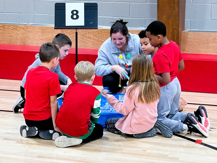 A group of students sit in a circle with adult during winter carnival activity. 