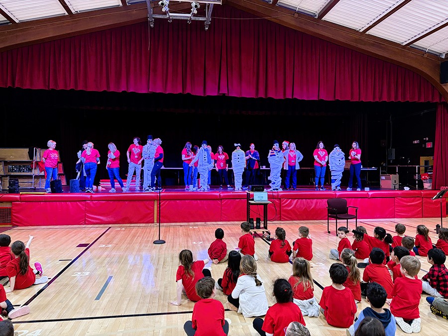 JES teachers compete in contest on stage with students sitting on the gym floor.